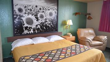 A hotel room with a large bed, a chair, a nightstand with a lamp, and a wall-mounted telephone.
