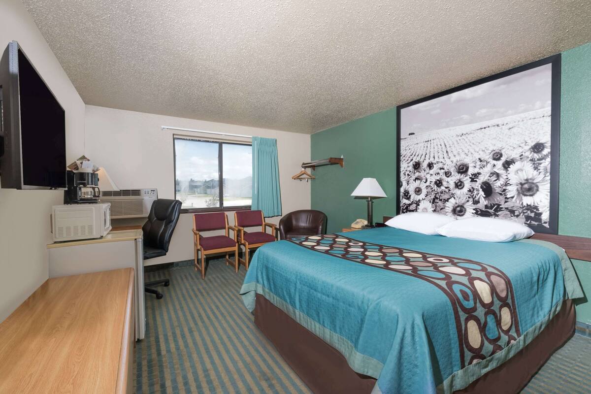 A hotel room with a bed, desk, chairs, and a large window.
