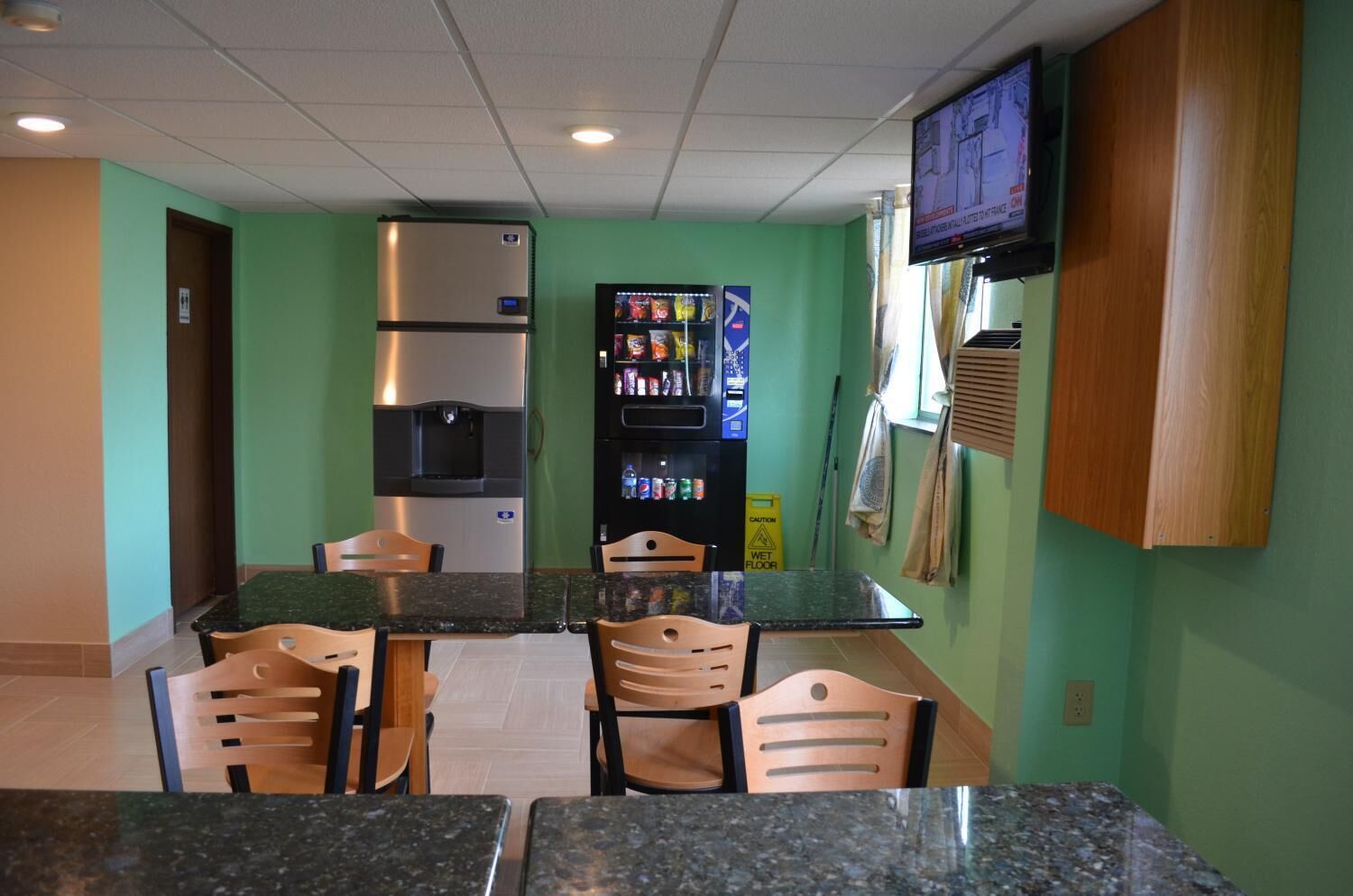 A small kitchenette with a refrigerator, microwave, and coffee machine. There are wooden chairs around a granite countertop.