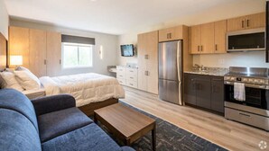 A compact living space with a bed, sofa, kitchenette, and a TV mounted on the wall.