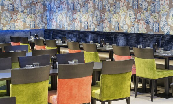 Interior de restaurante con varias mesas y sillas, pared con diseño y salpicadero de azulejos azules.