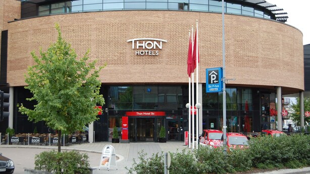 Ein modernes Hotel mit einer geschwungenen Ziegelaußenwand, einem markanten Eingang und einem sichtbaren Parkschild.