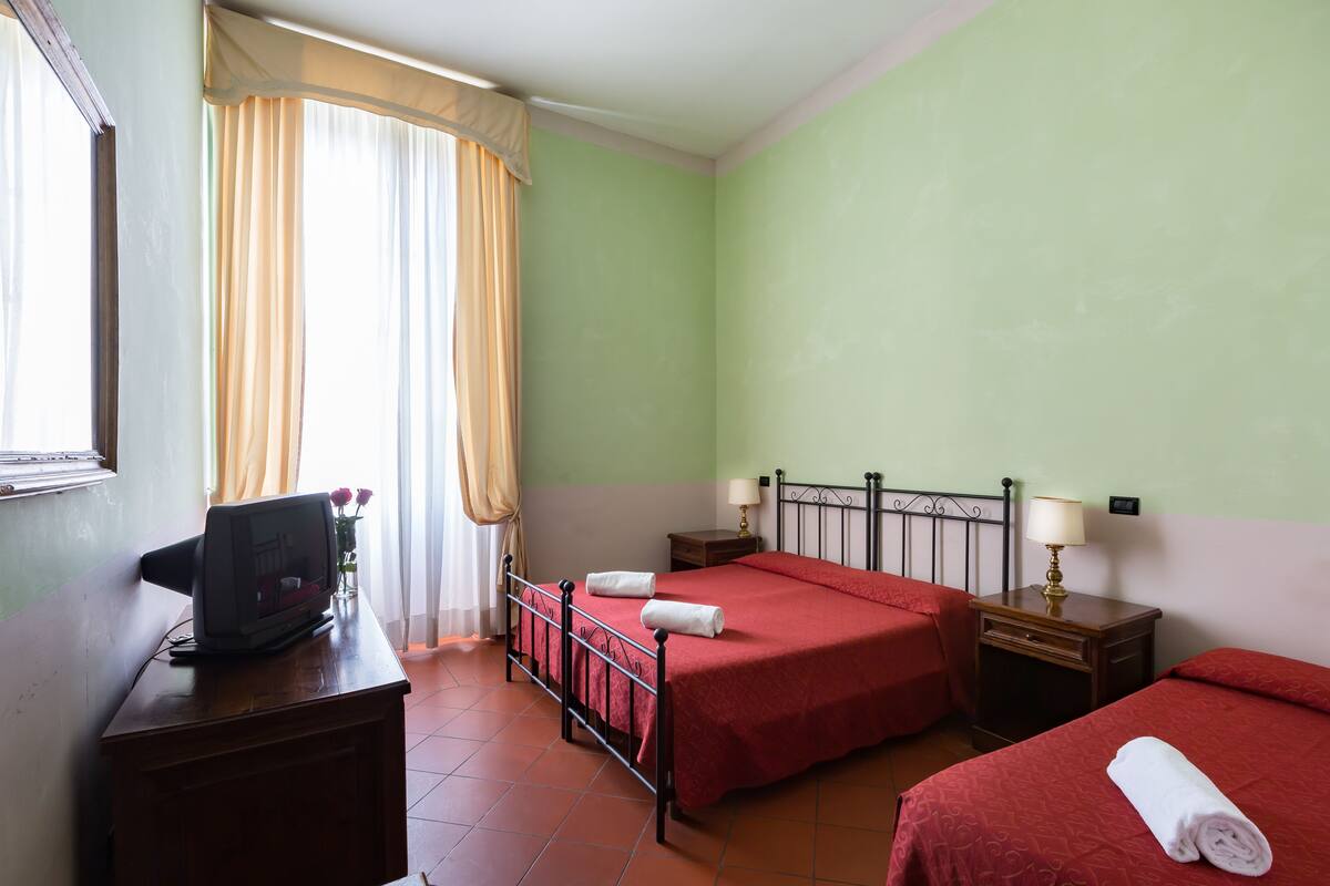 A hotel room with two beds, a desk with a television, and a window with curtains.