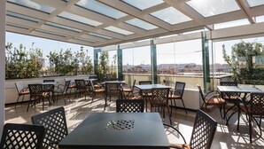 A rooftop terrace with tables and chairs, large windows, and a view of the city. - Domus Sessoriana (Rome)