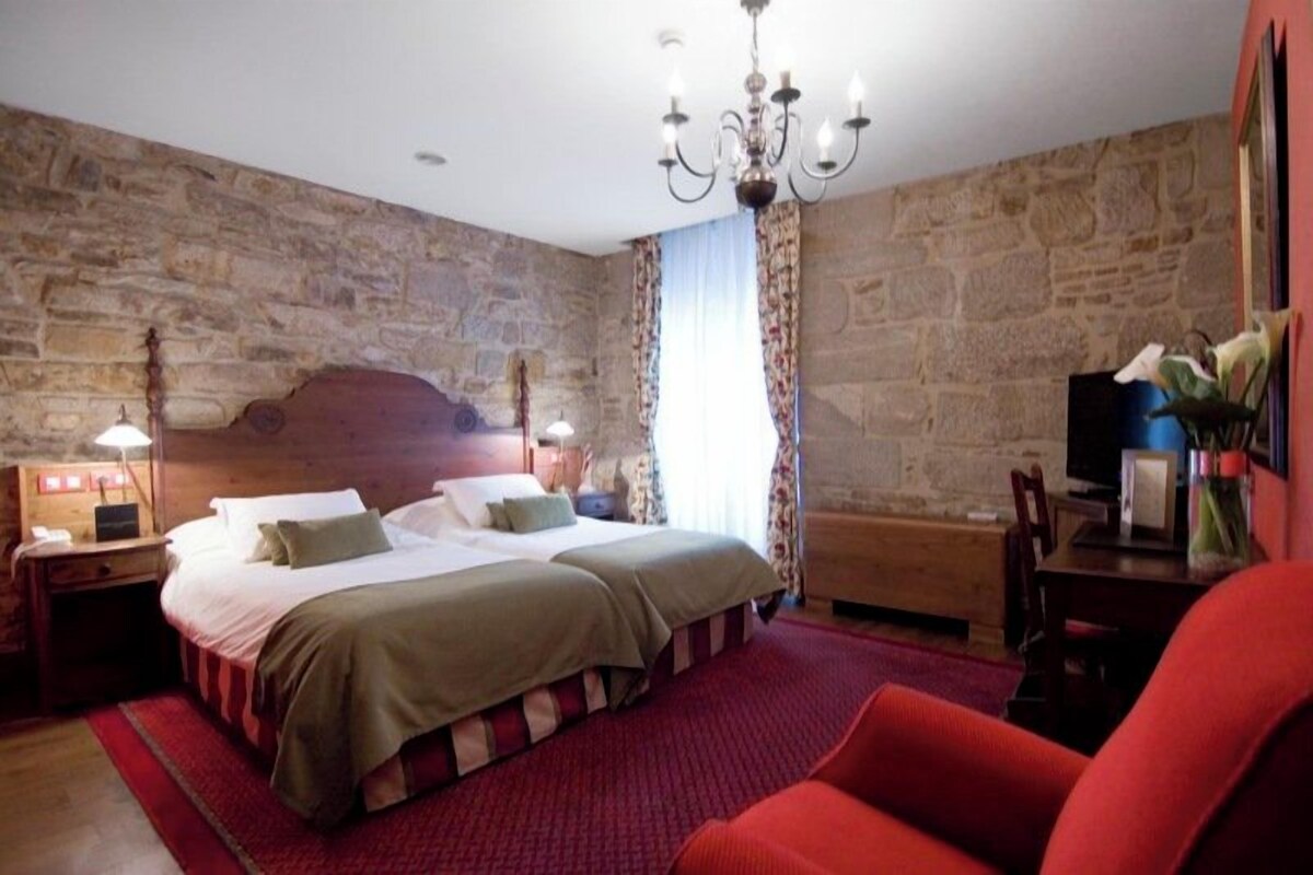 A bedroom with a stone wall, a bed with a wooden headboard, a red carpet, and a chandelier.