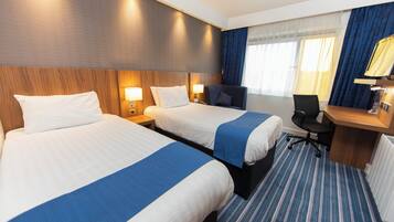 A hotel room with two beds, a desk, a chair, and a window with curtains.