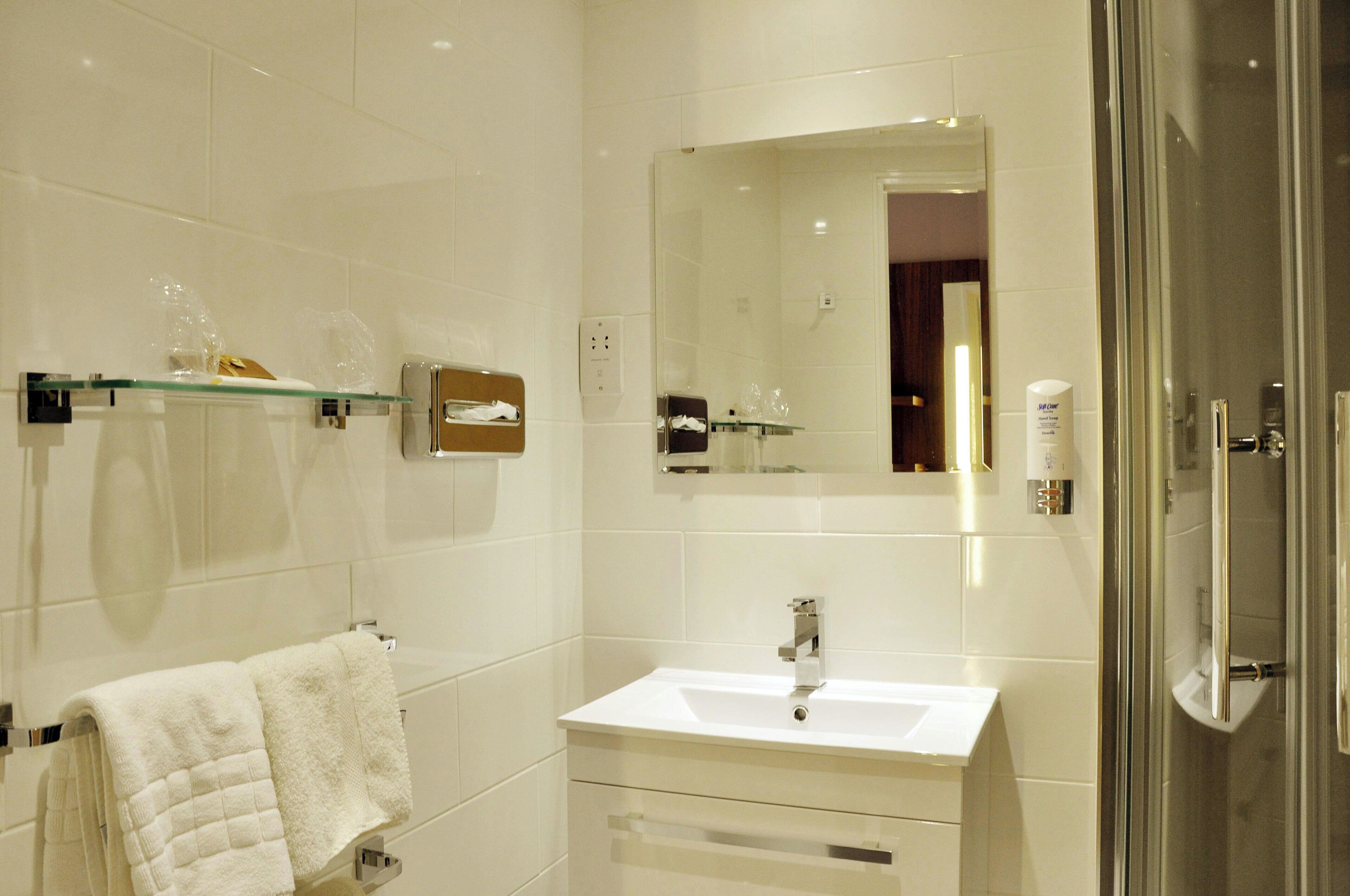 A modern bathroom with a white sink, a glass shower enclosure, and a mirror above the sink.