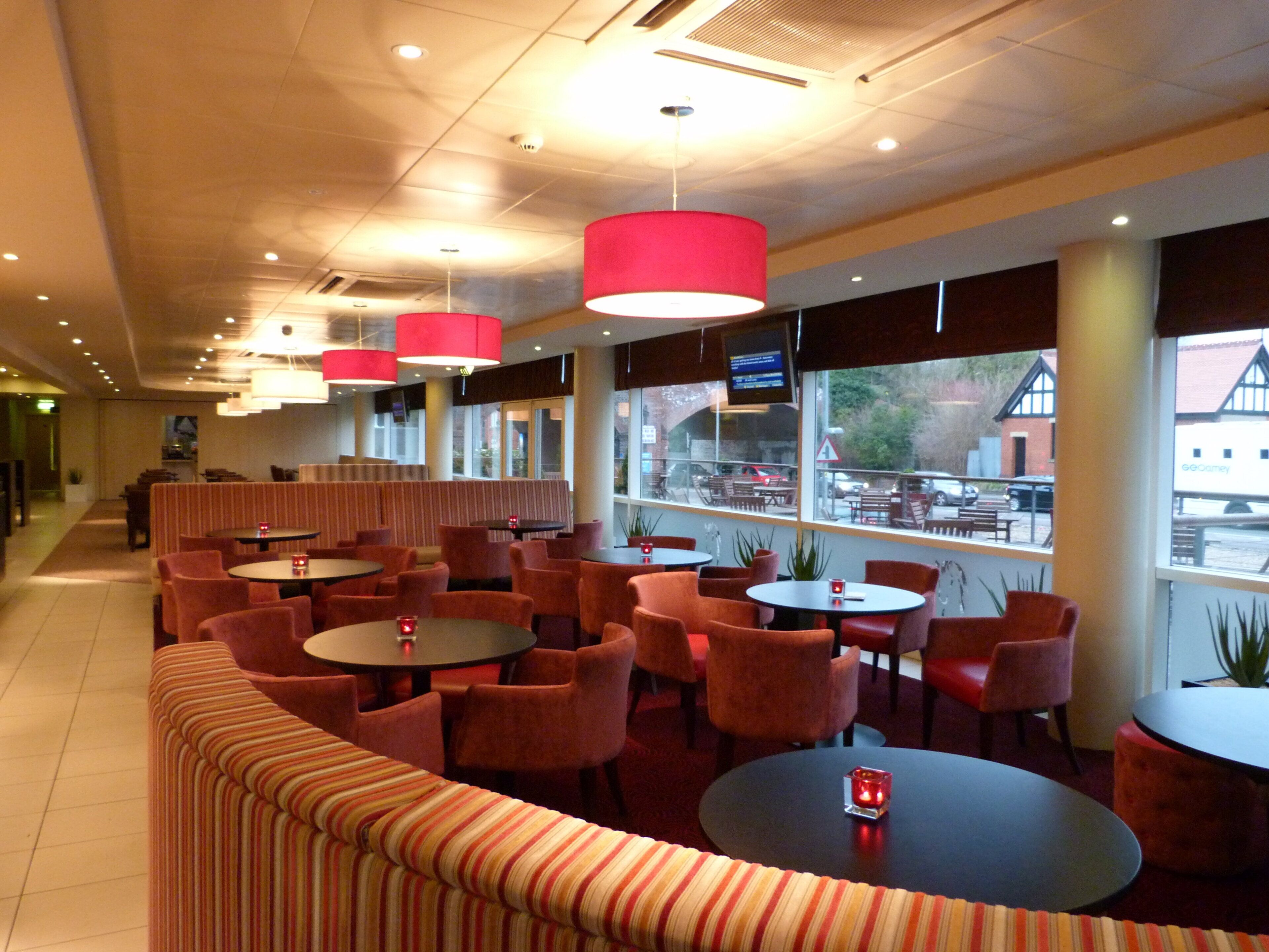 A restaurant interior with round tables, red chairs, and a striped sofa.