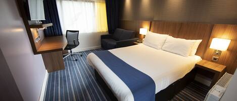 Habitación de hotel con una cama grande, un escritorio, una silla, un televisor y un ventanal con cortinas.