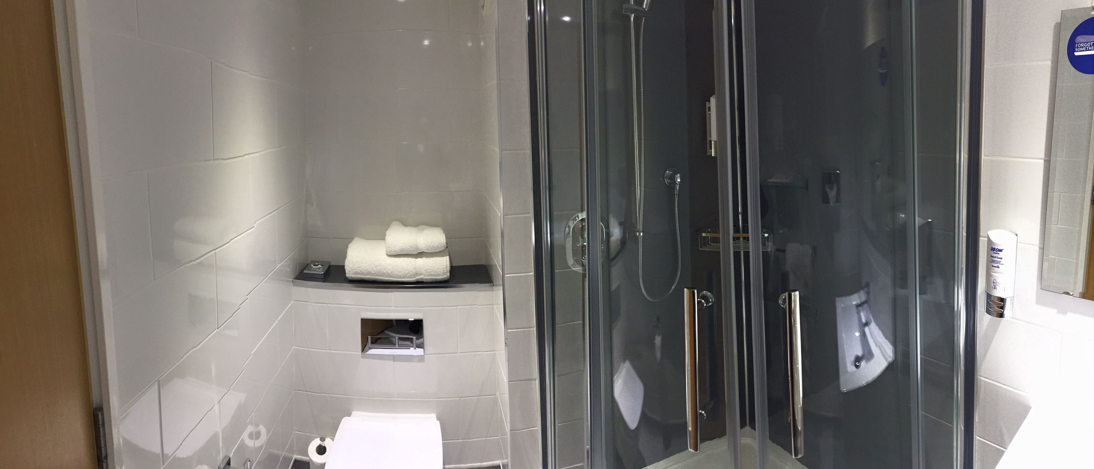 A modern bathroom with a glass-enclosed shower, a toilet, and a small shelf with a towel.