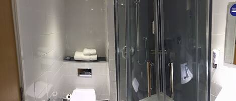 Un baño moderno con ducha de vidrio, inodoro y un pequeño estante con una toalla.