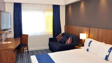 A hotel room with a bed, a desk, a chair, a TV, and a window with curtains.