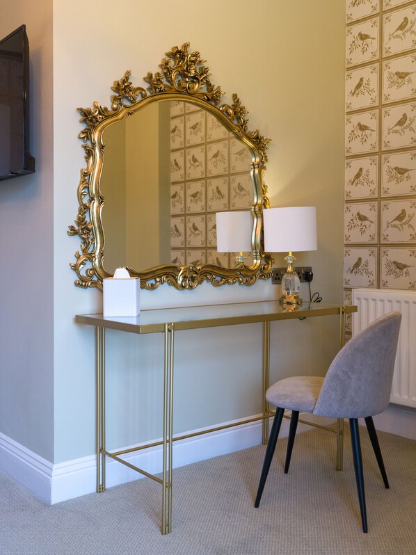 A room with a vanity table, a mirror with an ornate gold frame, a chair, and a lamp. - The Riverside, WorldHotels Distinctive (Salisbury)
