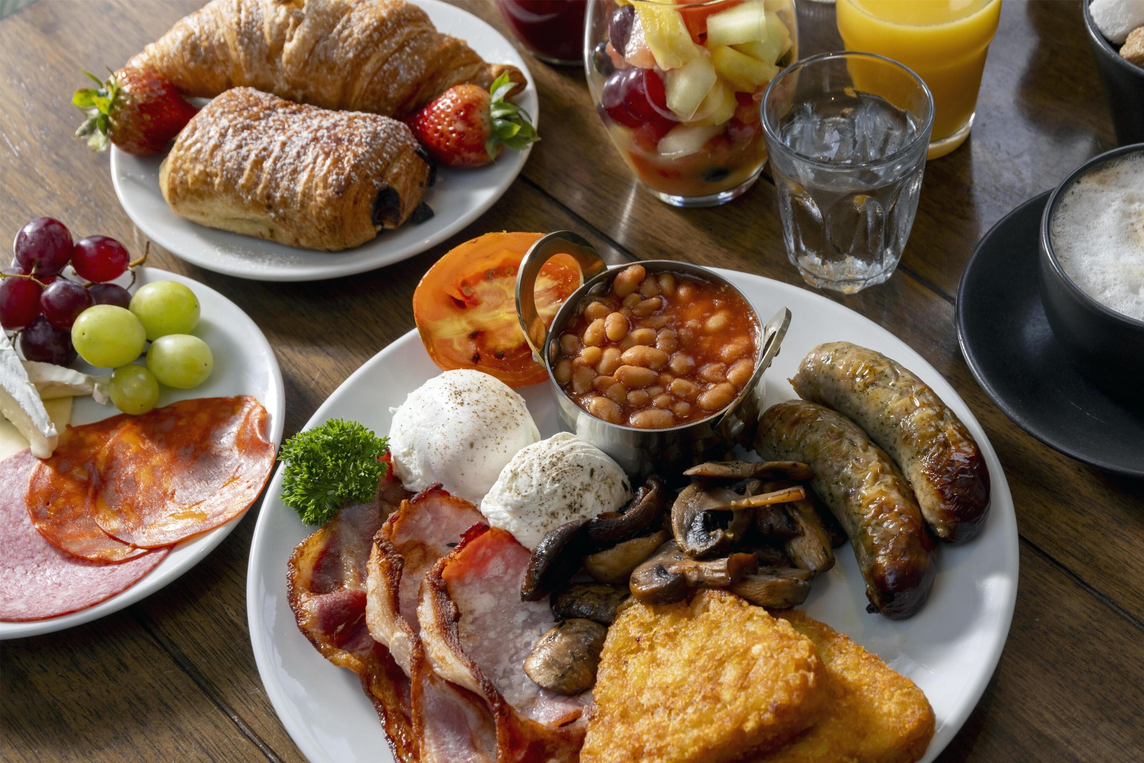 A breakfast plate with eggs, sausages, bacon, mushrooms, toast, and a side of beans.