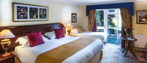 A hotel room with two beds, a window with curtains, a small table with a vase, and a patterned carpet.