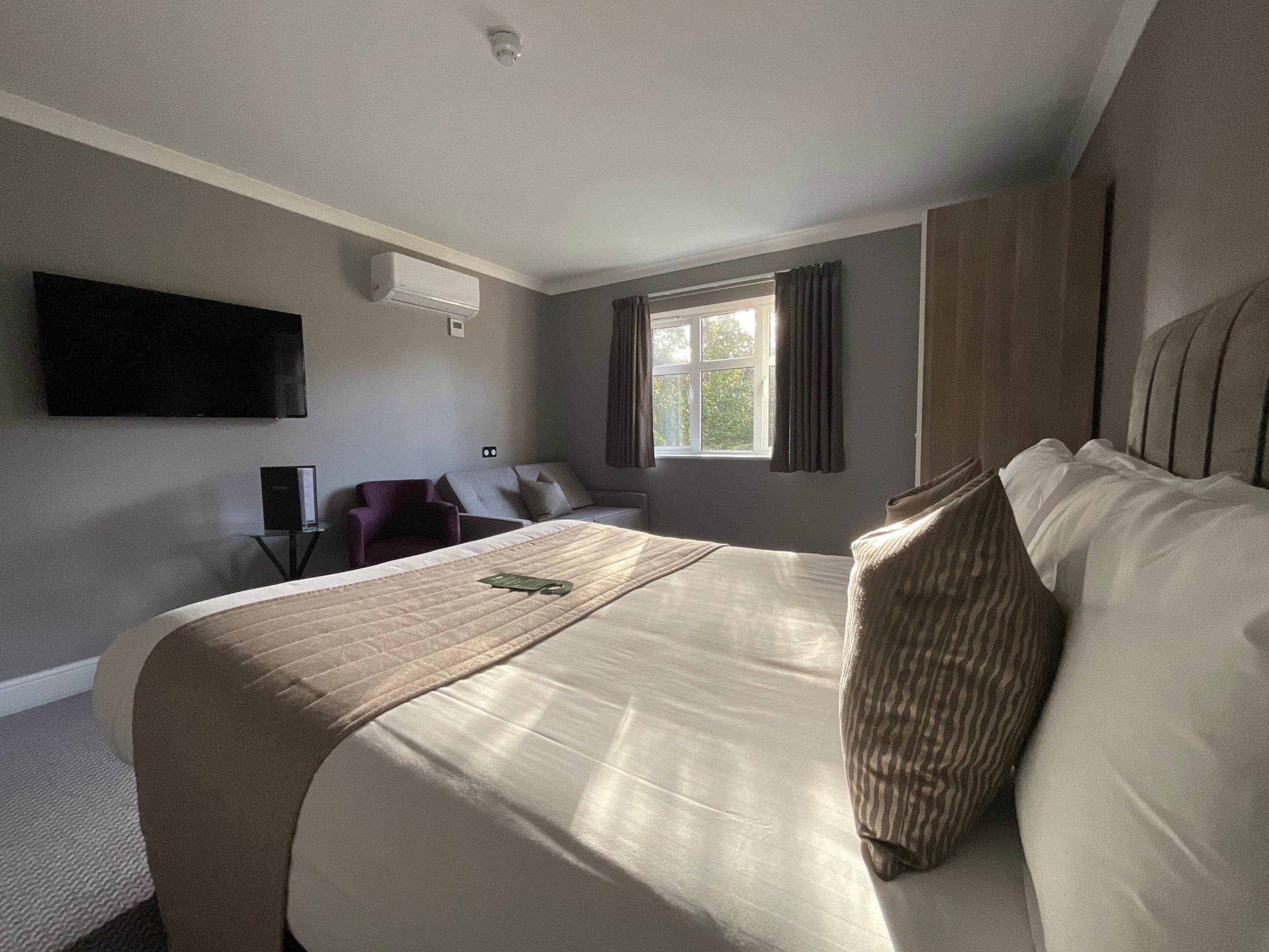 Habitación de hotel con una cama grande, un televisor de pantalla plana montado en la pared, una ventana con cortinas y un equipo de aire acondicionado.