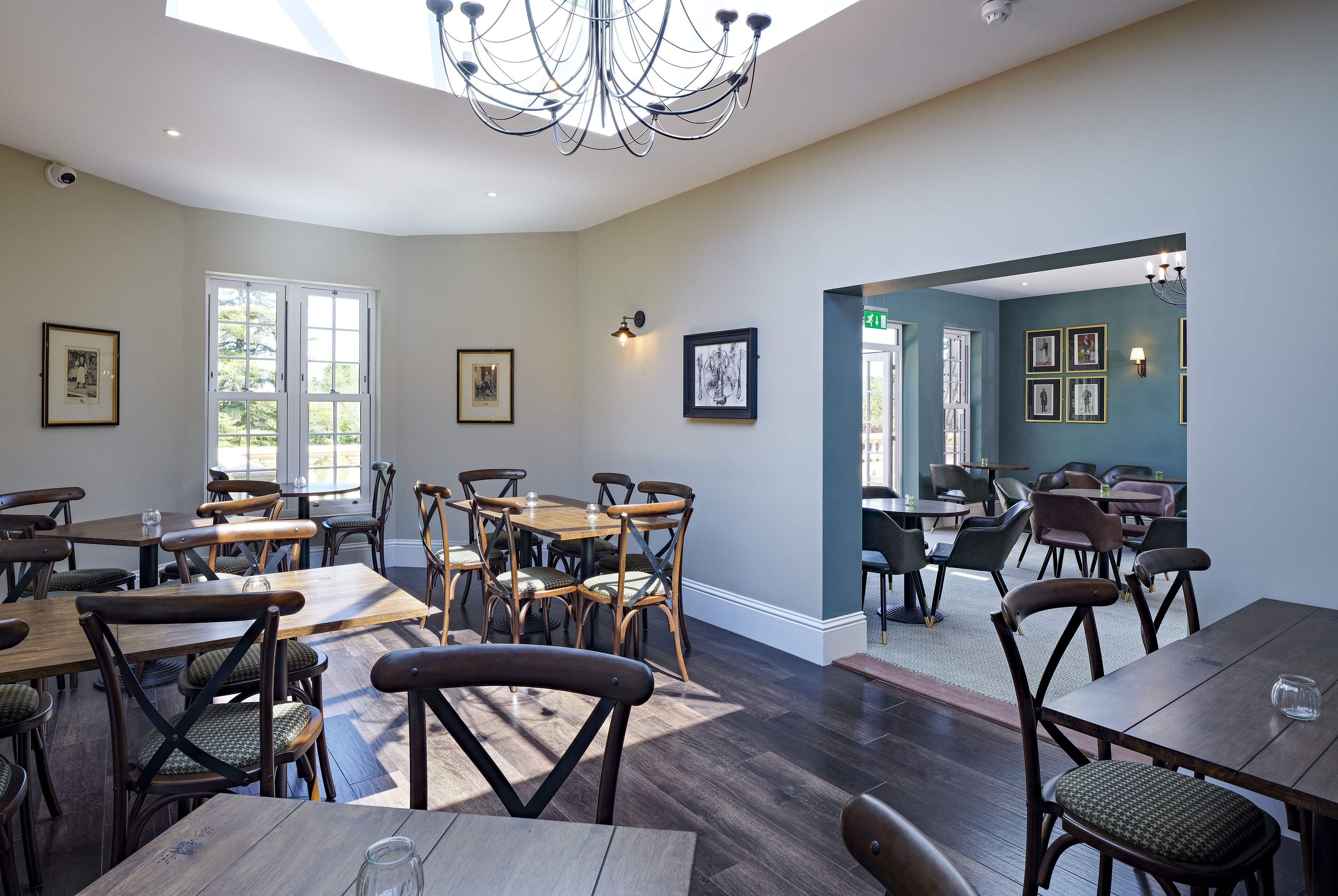 A dining area with wooden tables and chairs, framed artwork on the walls, and a chandelier.