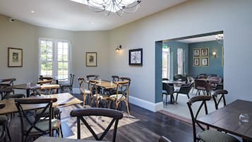 A dining area with wooden tables and chairs, framed artwork on the walls, and a chandelier.