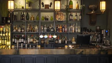 Un espace bar avec des étagères remplies de bouteilles d’alcool, une machine à café et des tabourets de bar.