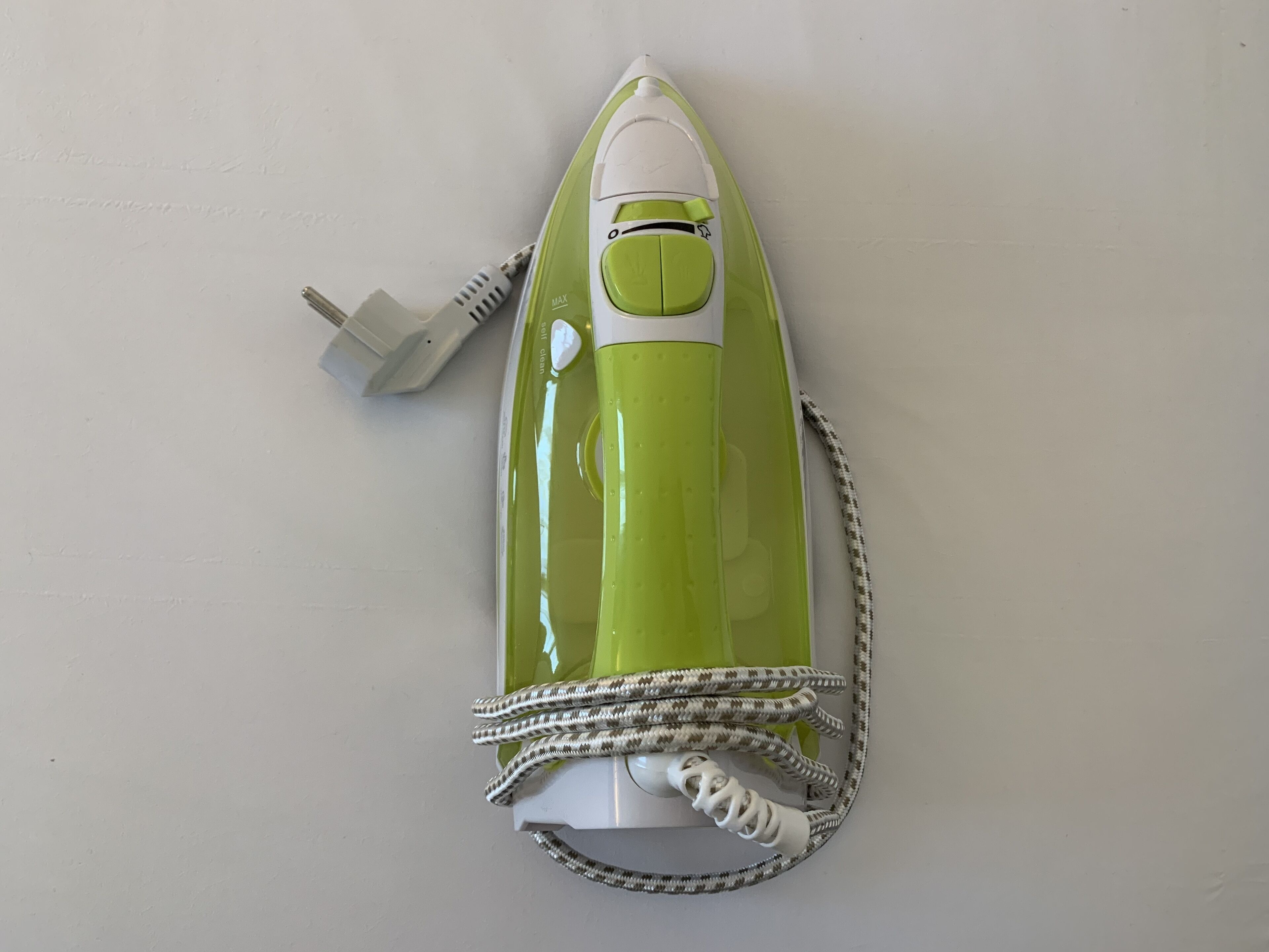 A green and white iron with a power cord coiled around it, placed on a white surface.