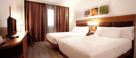 A hotel room with two beds, a desk with a TV, and a window with curtains.