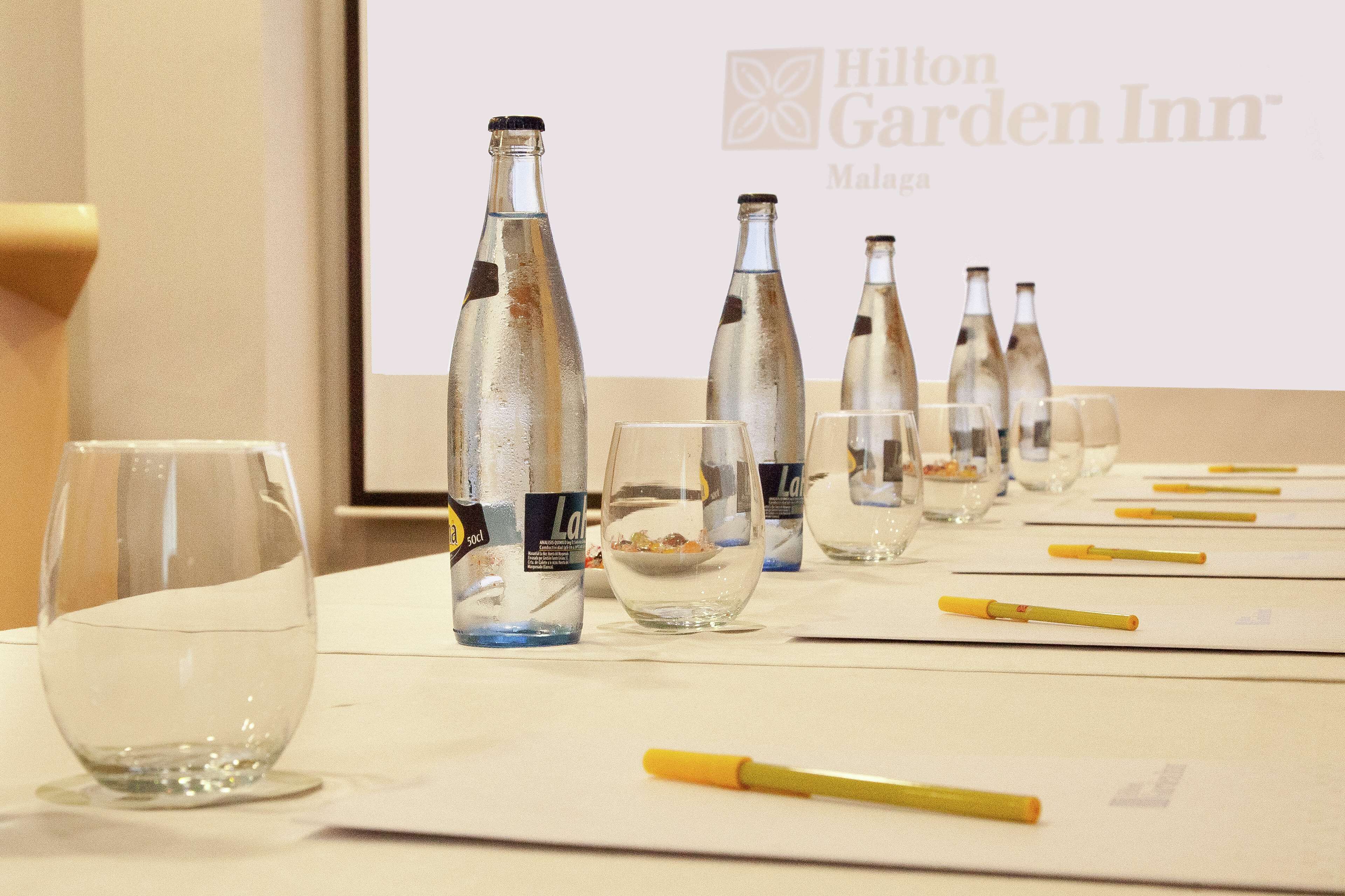 Una mesa con vasos y botellas vacías, un bolígrafo amarillo y una pantalla mostrando el logotipo de Hilton Garden Inn.