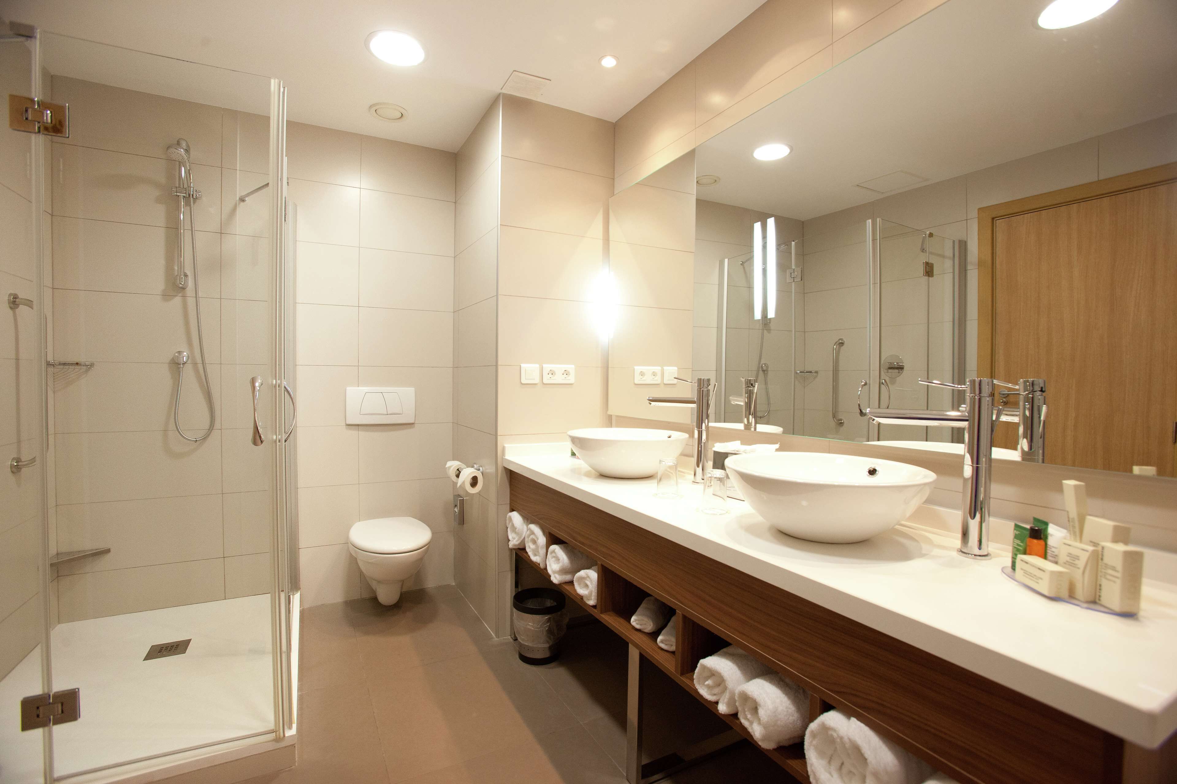 Een moderne badkamer met een glazen douchecabine, toilet, wastafel met grote spiegel en netjes opgevouwen handdoeken.