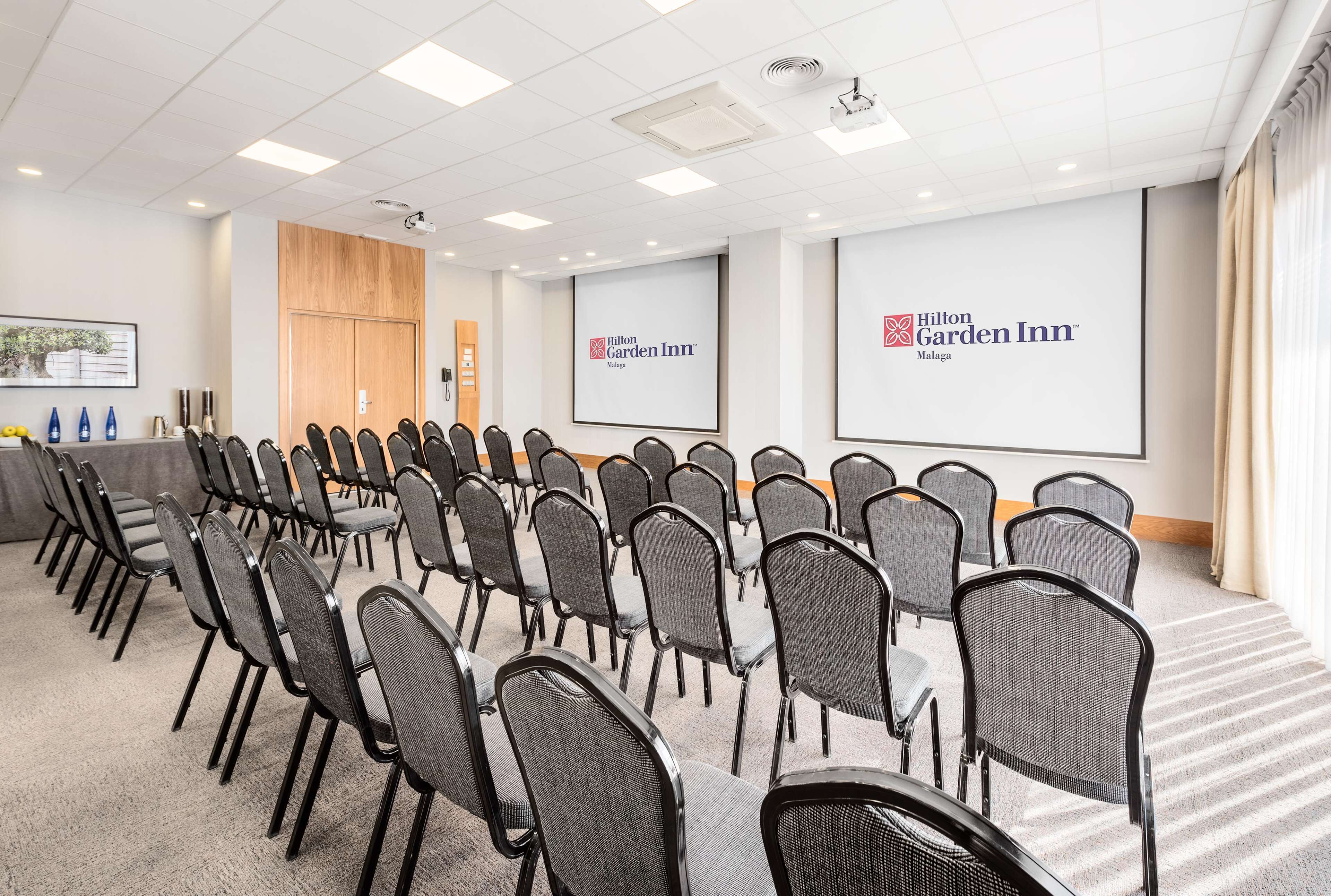 A conference room with rows of chairs, a projector screen, and a large screen displaying the Hilton Garden Inn logo.