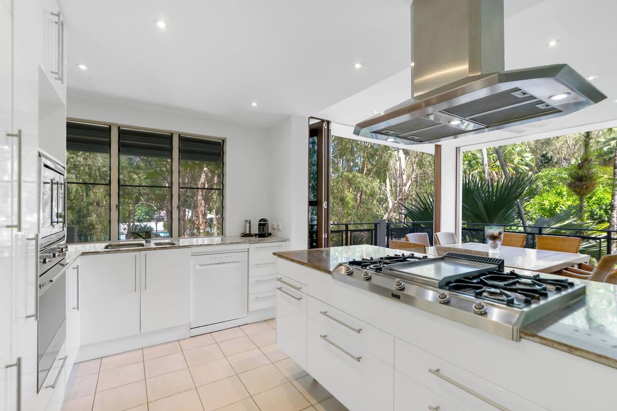 Een moderne keuken met witte kastjes, een groot eiland met een gasfornuis en uitzicht op groen.