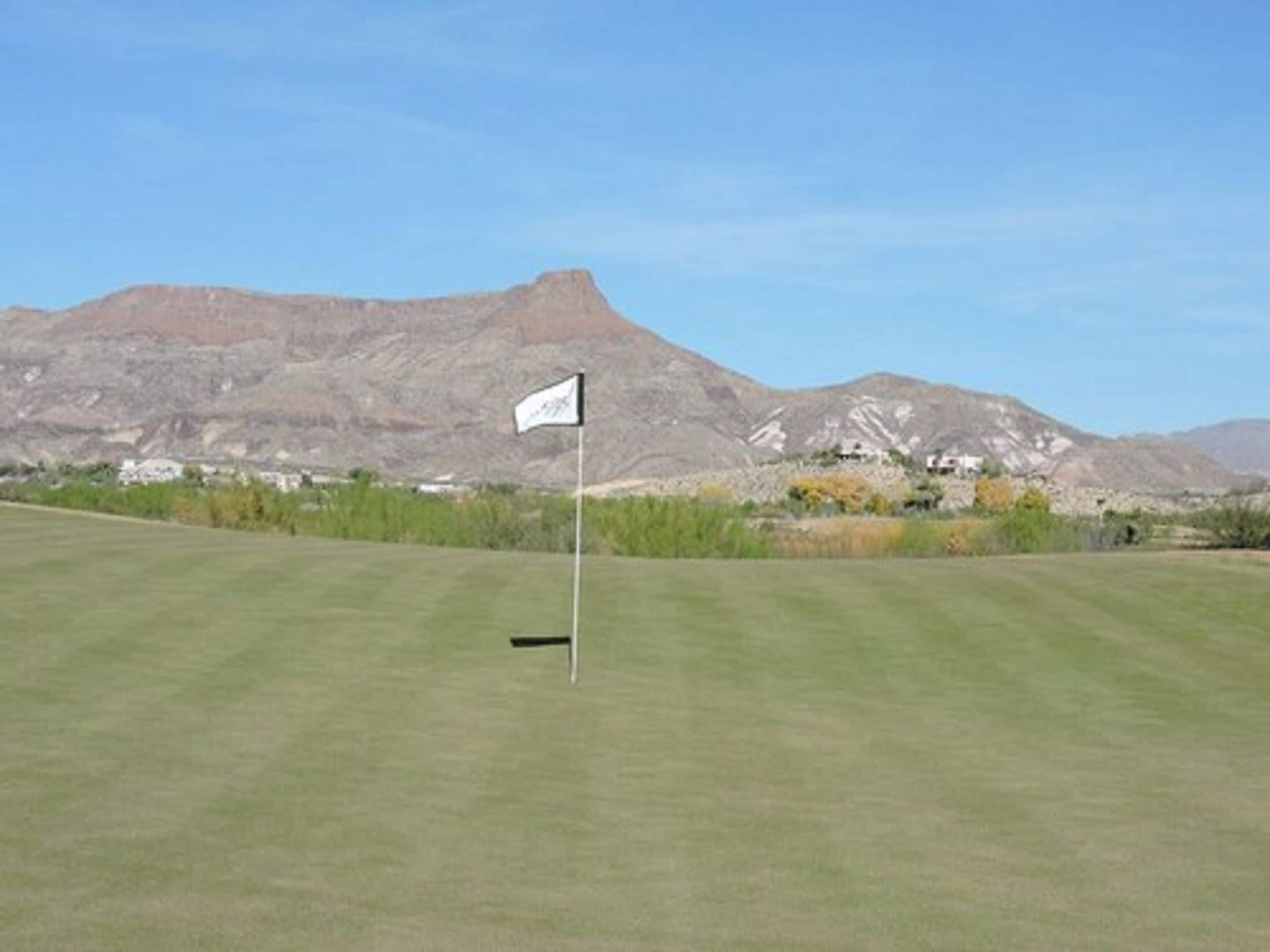 A golf course with a flagstick in the foreground and mountains in the background.