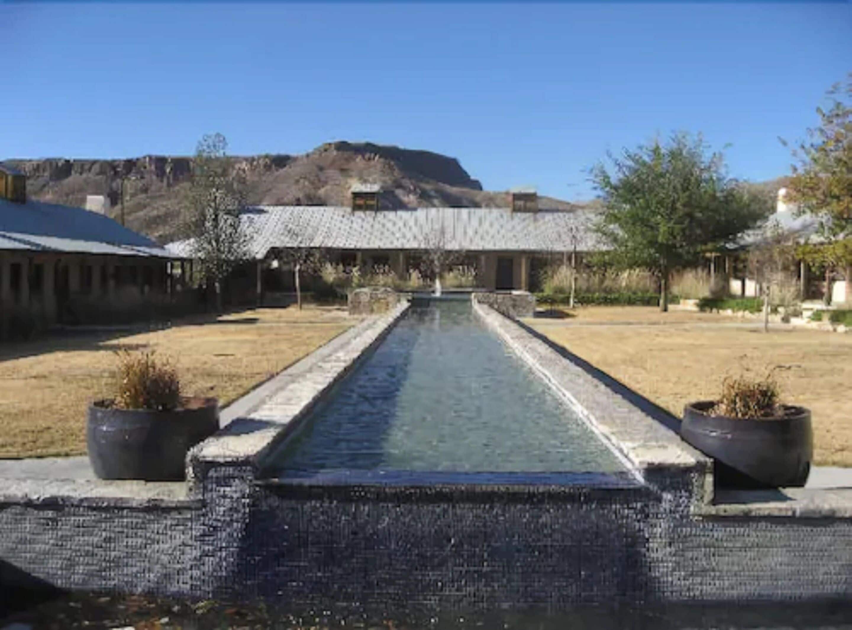 A pool with a stone border, surrounded by a grassy area and potted plants.