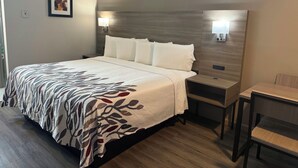 A hotel room with a large bed, bedside tables, a desk, and a chair. - Red Roof Inn Orangeburg (Orangeburg)