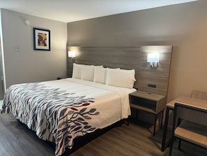 A hotel room with a large bed, bedside tables, a desk, and a chair. - Red Roof Inn Orangeburg (Orangeburg)