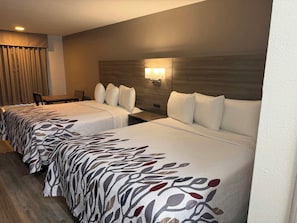 Habitación de hotel con dos camas, un escritorio, una silla y una lámpara fijada a la pared.