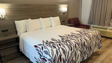A hotel room with a large bed, two wall-mounted lights, a red chair, and a window with curtains.