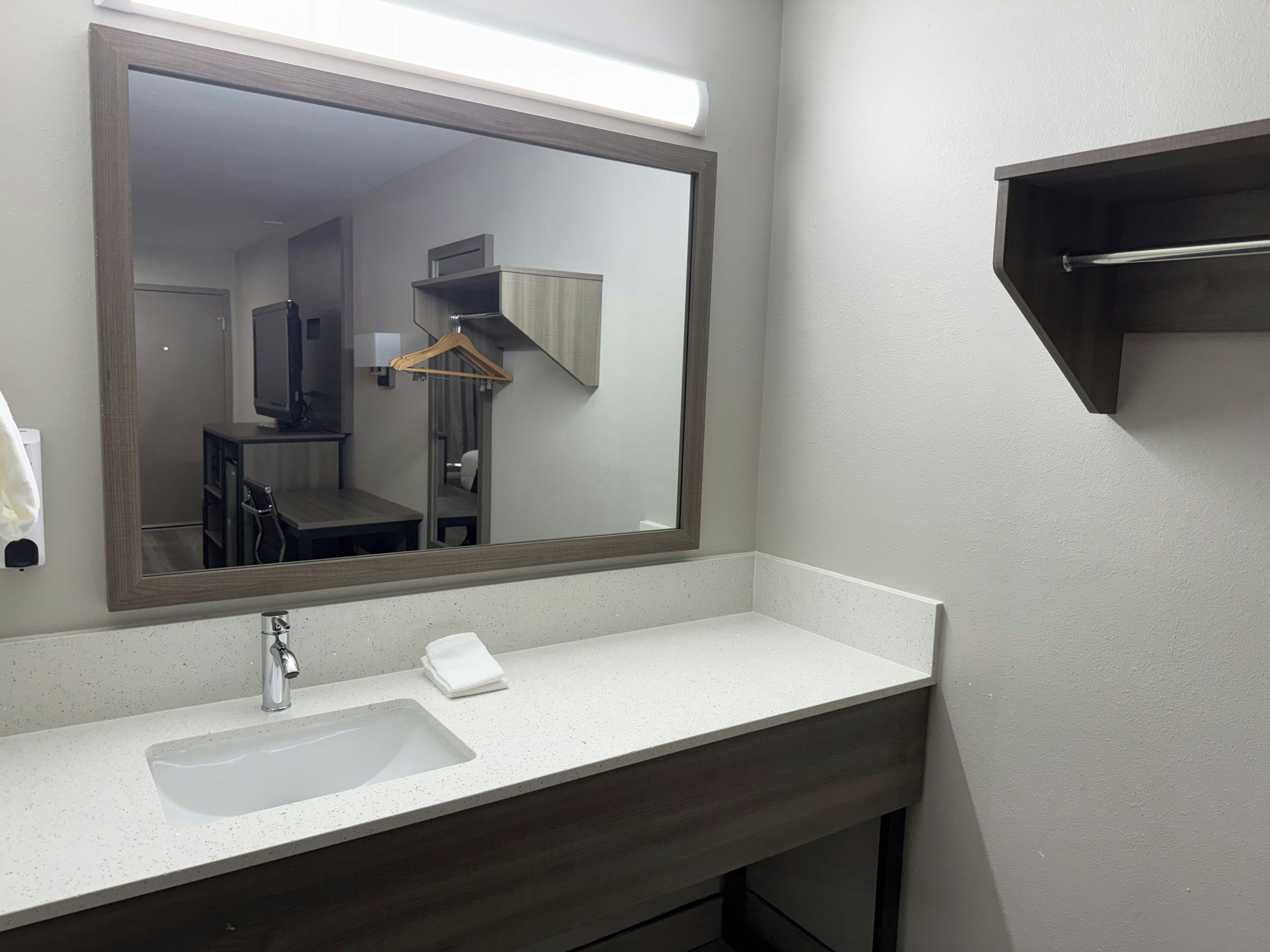 A bathroom with a large mirror, a sink, and a towel dispenser.
