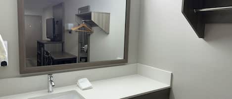 A bathroom with a large mirror, a sink, and a towel dispenser.