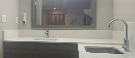 A bathroom with a large mirror, a sink, a faucet, and a towel rack.