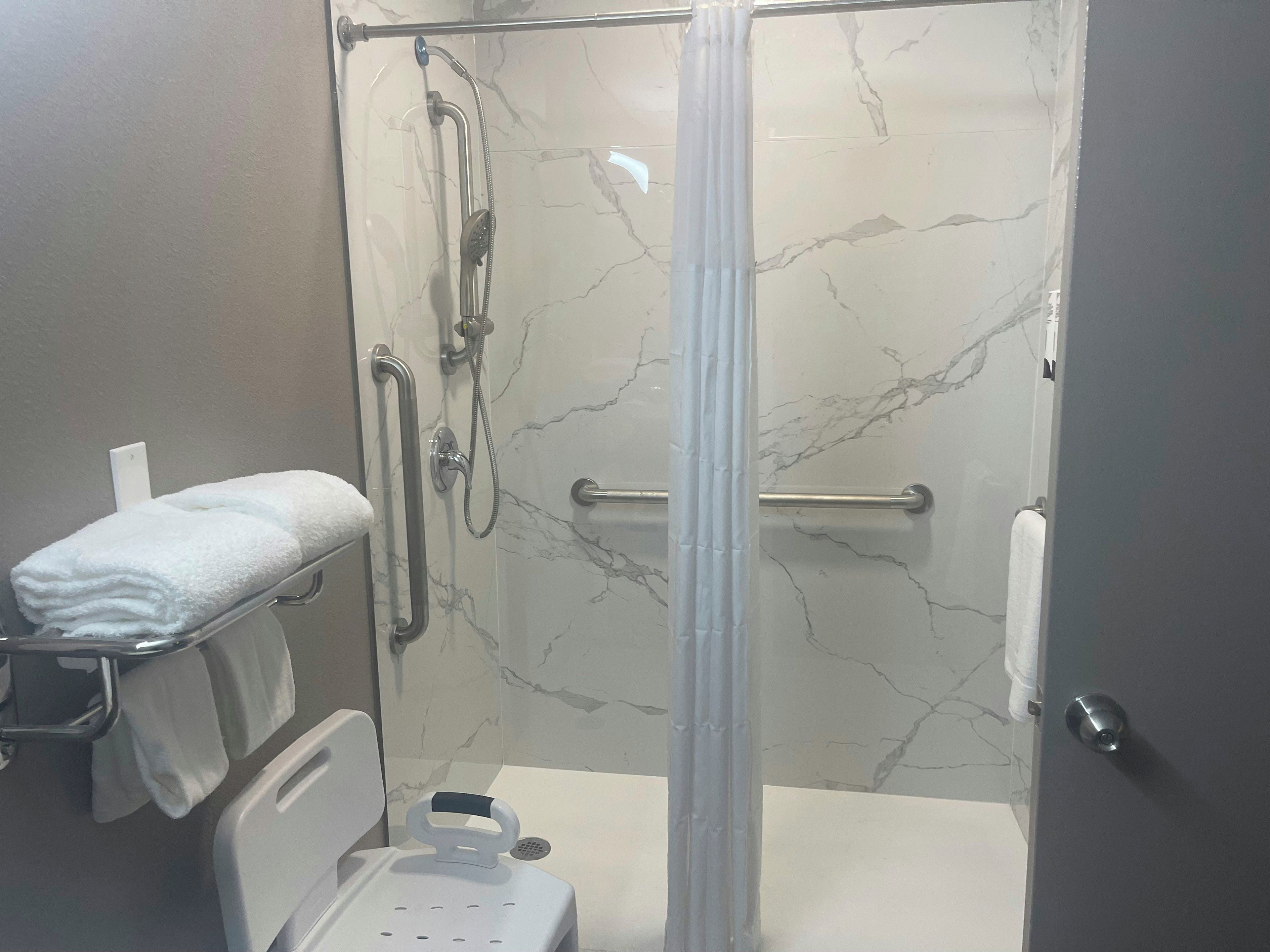 A shower with a glass door, a handrail, and a towel rack with towels.
