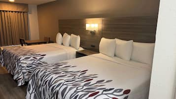Habitación de hotel con dos camas, un escritorio, una silla y una lámpara fijada a la pared.