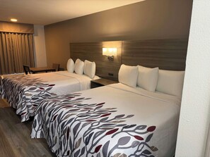 A hotel room with two beds, a desk, a chair, and a wall-mounted lamp.
