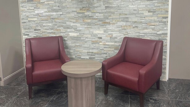 A Red Roof Inn with two red leather armchairs and a small wooden table in front of a stone-patterned wall. - Red Roof Inn Orangeburg (Orangeburg)