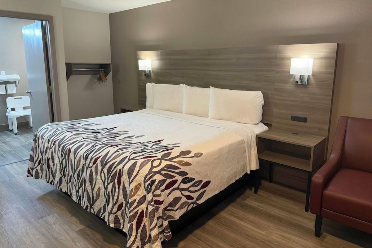 A hotel room with a bed, bedside tables, a chair, and a wall-mounted light fixture.
