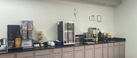 A hotel reception area with a counter, coffee machines, and a refrigerator.