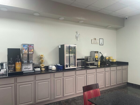 Un espace d’accueil d’hôtel comprenant un comptoir, des machines à café et un réfrigérateur.
