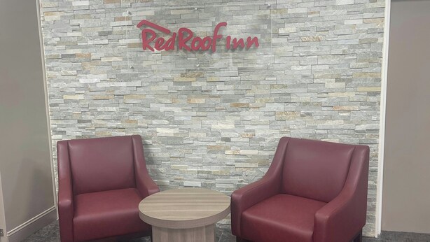 A Red Roof Inn with two red leather armchairs and a small wooden table in front of a stone-patterned wall. - Red Roof Inn Orangeburg (Orangeburg)
