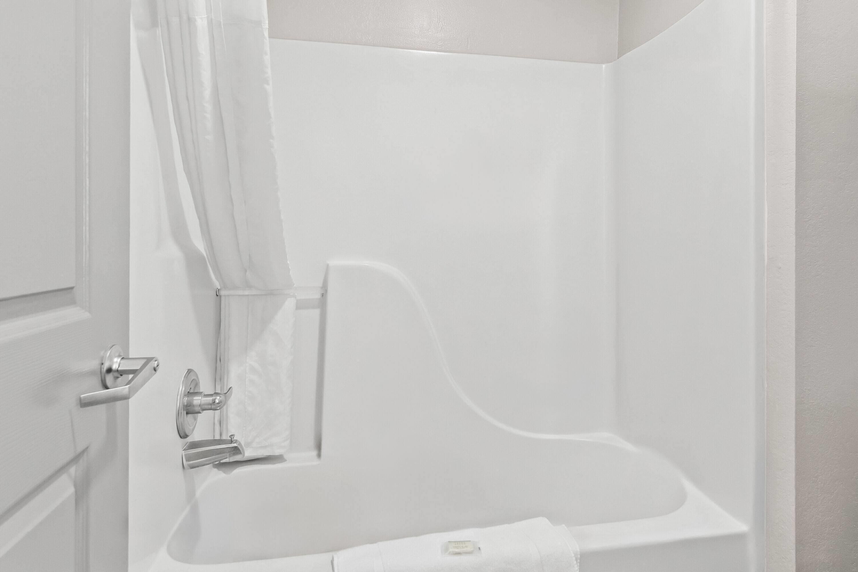 Un baño blanco con una bañera, una cortina de ducha y una toalla colgada en la pared.