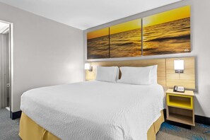 A hotel room with a large bed, a nightstand with a phone, and a wall-mounted light. - Days Inn by Wyndham Ocean Springs (Biloxi)
