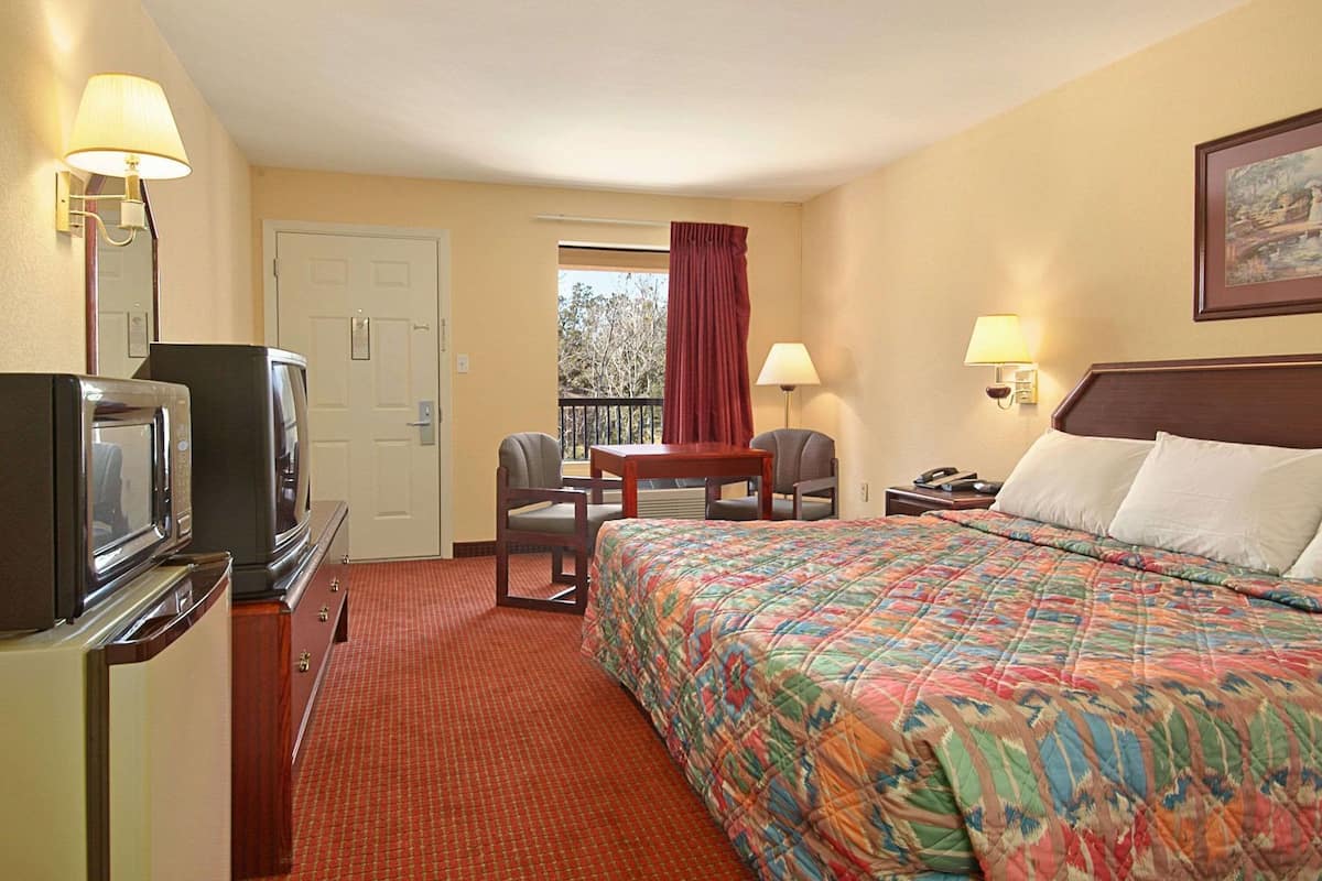 A hotel room with a bed, a desk, a chair, a television, and a window with curtains.