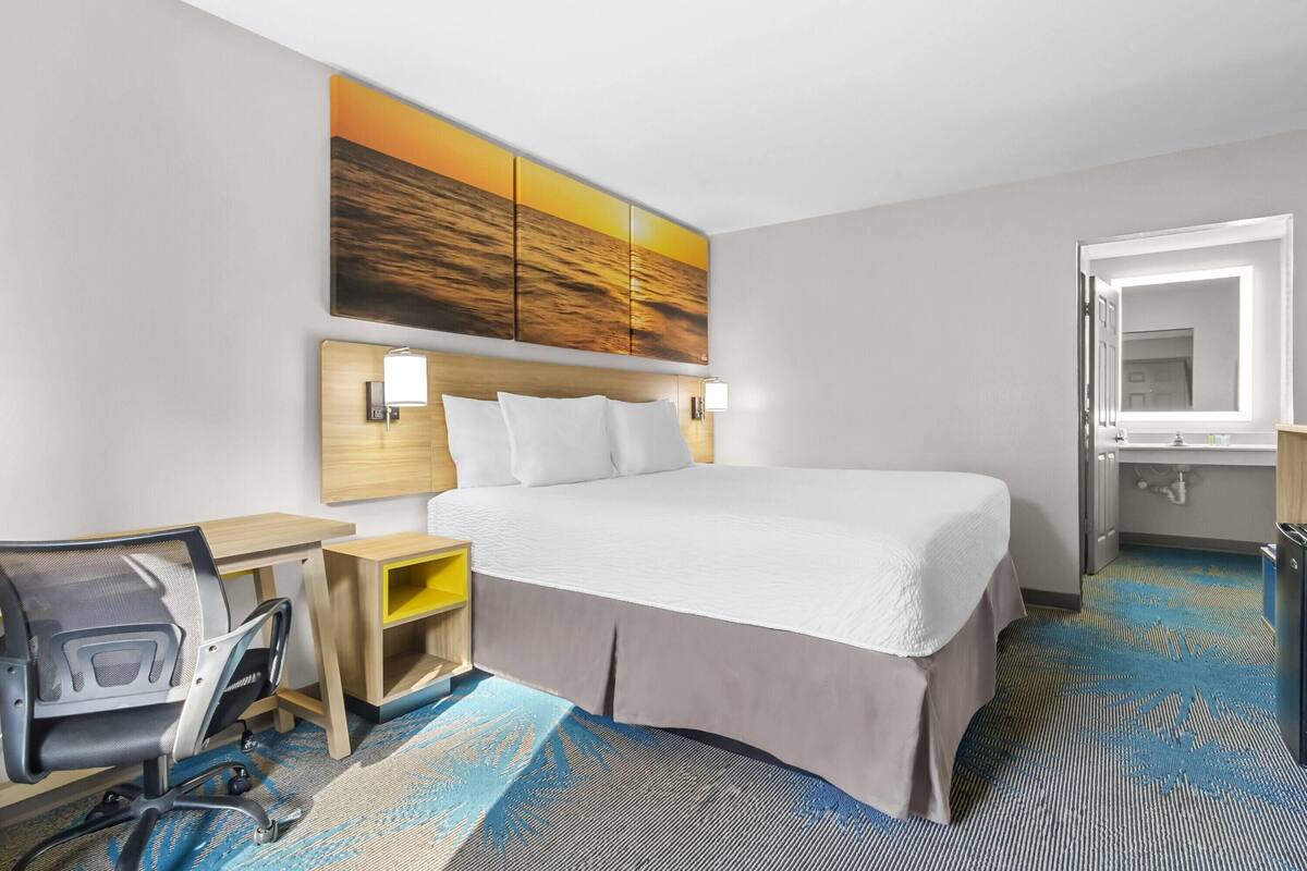 A hotel room with a bed, desk, chair, and a large painting on the wall.